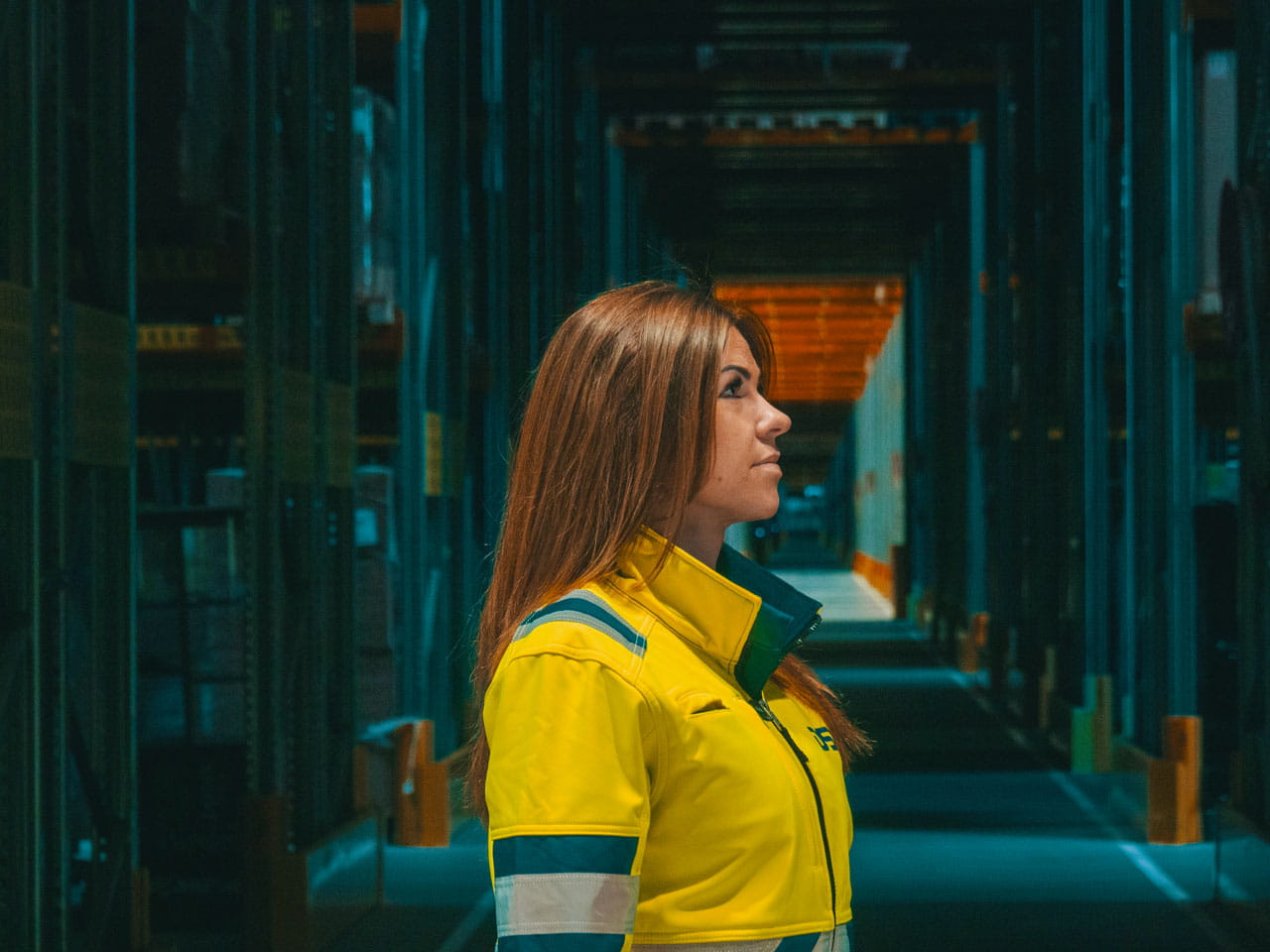 Side profile of a woman in a yellow high-visibility jacket standing in a warehouse